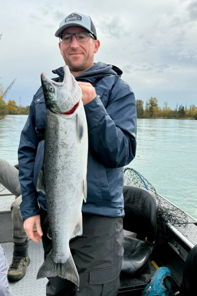 Angler holding a freshly caught silver salmon during a guided King of the River fishing trip on Alaska’s Kenai River.