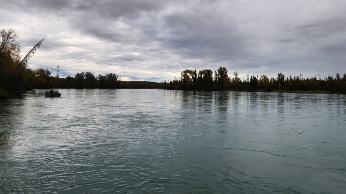 Peaceful view of the Kenai River with a fishing boat surrounded by nature and autumn colors in Alaska.