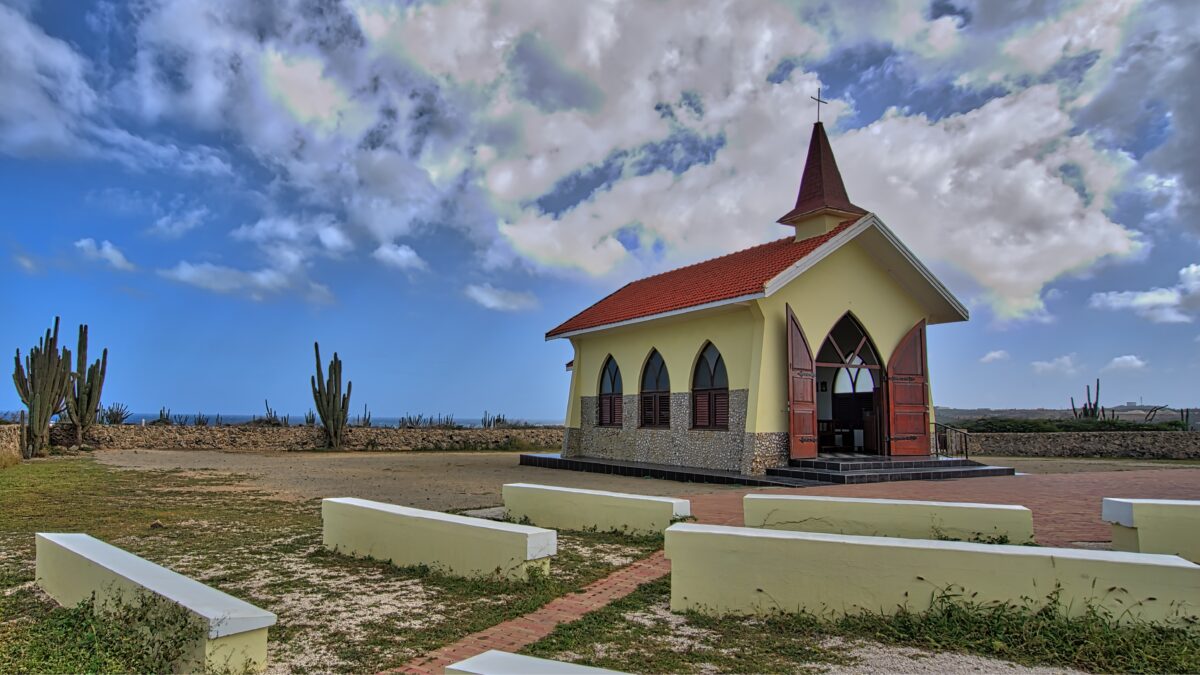 Alto Vista Chapel in Aruba with yellow facade, red roof, and desert landscape under a bright blue sky