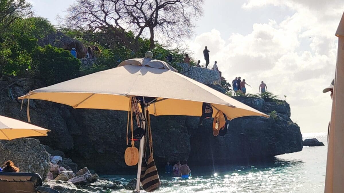 Cliff Jumping at Grote Knip Beach Curaçao | Dohrn Travels People cliff jumping into the water at Grote Knip Beach in Curaçao with umbrellas and rocky shoreline