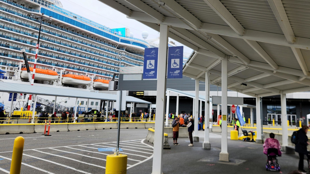 Covered passenger entrance at Seattle Pier 91 cruise terminal with cruise ship in the background.