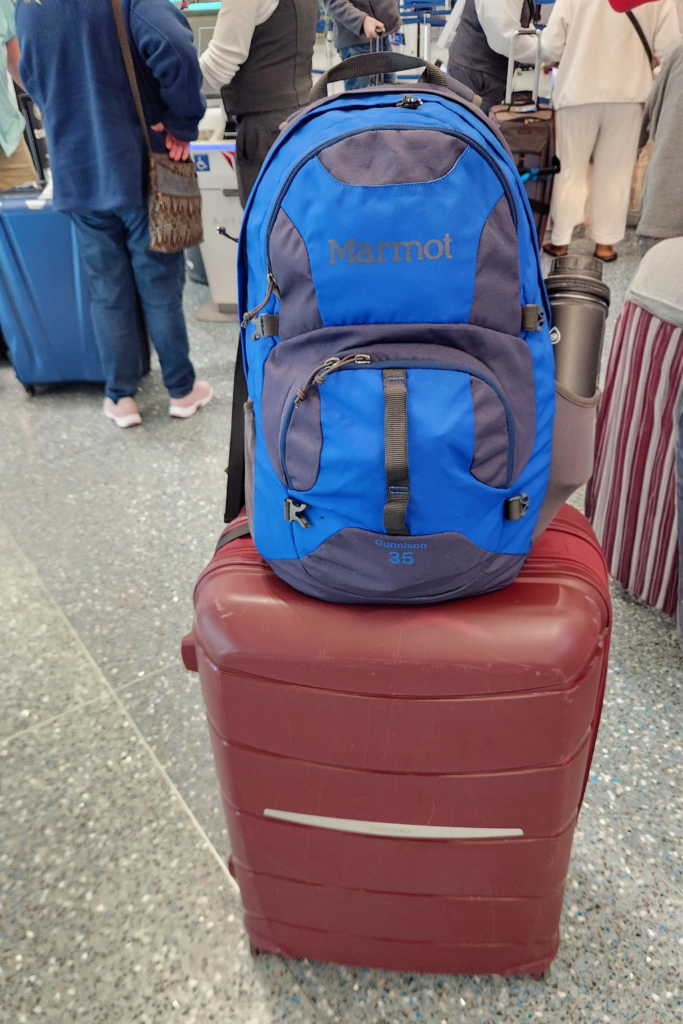 Alaska Cruise Daypack and Luggage at the Airport | Dohrn Travels Blue daypack sitting on top of a suitcase at the airport before an Alaska cruise.