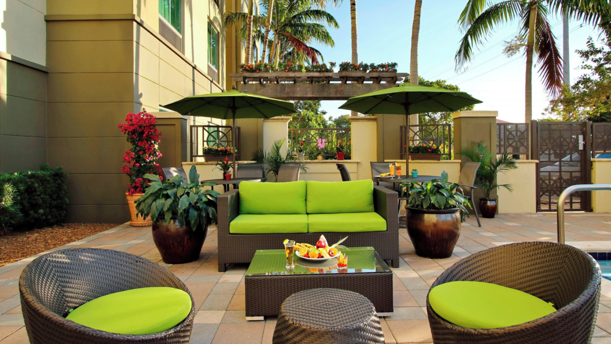 Outdoor patio at Fairfield by Marriott Fort Lauderdale Airport with lounge seating, umbrellas, tropical plants, and pool access
