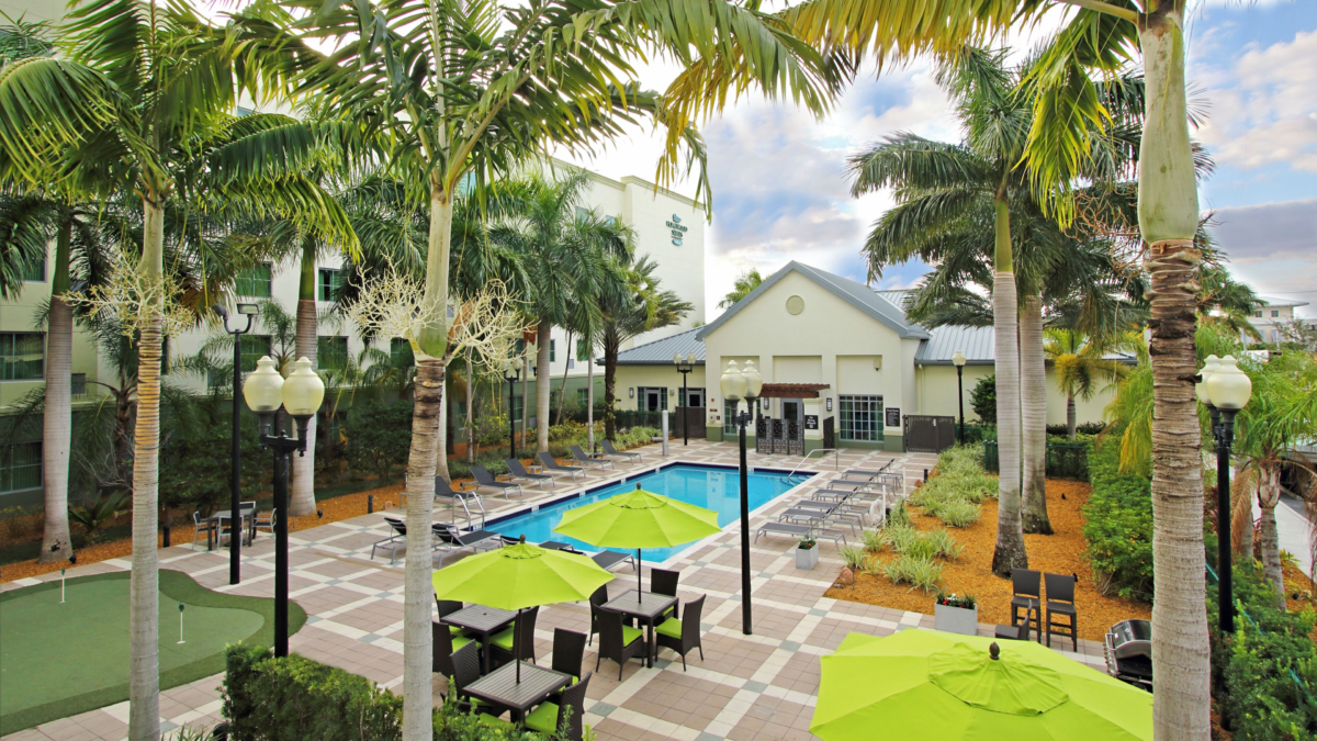 Outdoor pool and patio area at Homewood Suites Fort Lauderdale Airport with palm trees, lounge chairs, and putting green