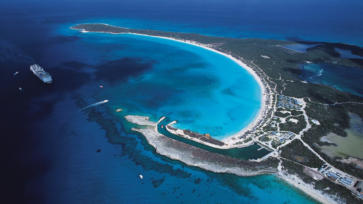 Aerial view of Half Moon Cay in the Bahamas, featuring its curved white-sand beach, turquoise water, and a cruise ship anchored offshore.