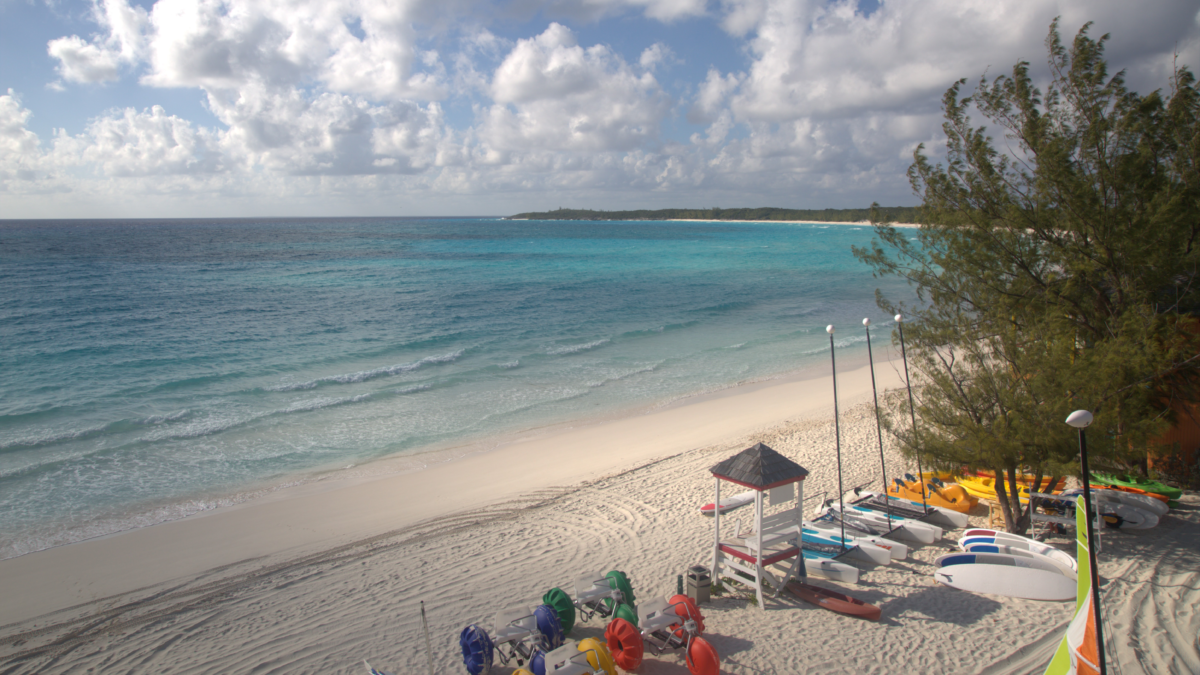 Elevated view of Half Moon Cay's white-sand beach and turquoise water, with sailboats, kayaks, and beach equipment along the shoreline.