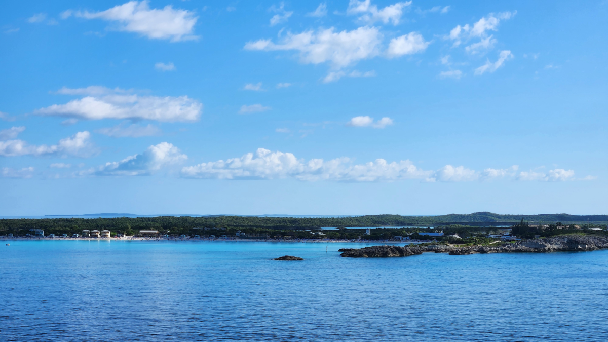 View of Half Moon Cay in the Bahamas from a Holland America cruise ship, showing the rocky shoreline, calm blue water, and island in the distance.